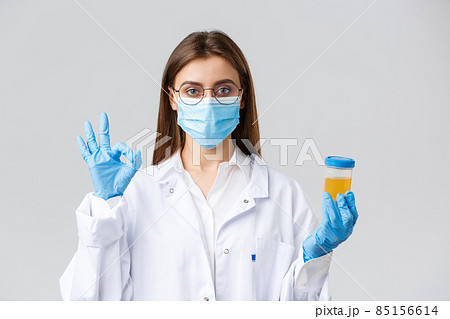 Covid-19, medical research, healthcare workers and quarantine concept. Professional doctor in scrubs, medical mask and gloves, holding patient urine sample and show okay sign, approve, making tests 85156614
