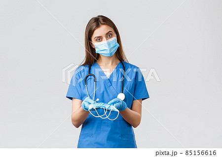 Covid-19, preventing virus, health, healthcare workers and quarantine concept. Attractive female nurse in blue scrubs and personal protective equipment, giving medical masks to patient 85156616