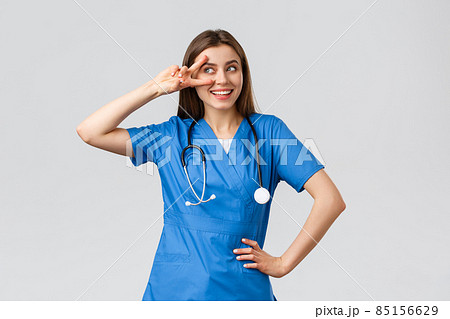 Medical workers, healthcare, covid-19 and vaccination concept. Cheerful and energized young female doctor, pretty nurse in blue scrubs, stethoscope, show peace near eye and smiling upbeat 85156629