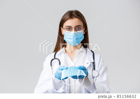 Covid-19, preventing virus, clinic, healthcare workers and quarantine concept. Young doctor in medical mask and gloves, white scrubs, giving face mask protection to patients, look serious 85156632