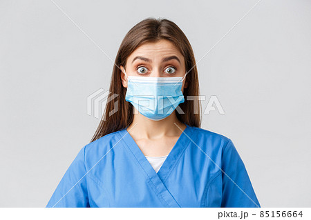 Covid-19, preventing virus, health, healthcare workers and quarantine concept. Surprised female nurse or doctor in blue scrubs and medical mask, staring shocked and excited at camera 85156664