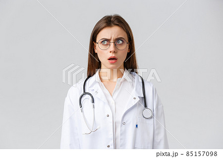 Healthcare workers, medicine, insurance and covid-19 pandemic concept. Shocked and confused young female doctor in white scrubs and glasses, stethoscope, stare left with concerned nervous face 85157098