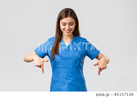 Healthcare workers, prevent virus, covid-19 test screening, medicine concept. Happy and pleased attractive female nurse or doctor, physician in blue scrubs, pointing looking down at advertisement Healthcare workers, prevent virus, covid-19 test screening, medicine concept. Happy and pleased attractive female nurse or doctor, physician in blue scrubs, pointing looking down at advertisement 85157136