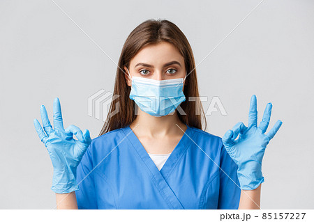 Covid-19, preventing virus, health, healthcare workers and quarantine concept. Professional female nurse or doctor in clinic, blue scrubs and medical mask, show okay sign, all under control Covid-19, preventing virus, health, healthcare workers and quarantine concept. Professional female nurse or doctor in clinic, blue scrubs and medical mask, show okay sign, all under control 85157227