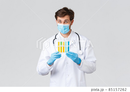 Hospital, healthcare workers, covid-19 treatment concept. Lab technician in laboratory trying find coronavirus vaccine, showing ampoules with samples, wearing medical mask and scrubs Hospital, healthcare workers, covid-19 treatment concept. Lab technician in laboratory trying find coronavirus vaccine, showing ampoules with samples, wearing medical mask and scrubs 85157262