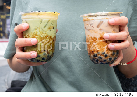 Cropped shot of woman holding a couple cup of iced Bubble tea (Milk tea and Green tea) in her hands. Bubble tea was a traditional drink in Taiwan before it became hugely popular all over the world. 85157496