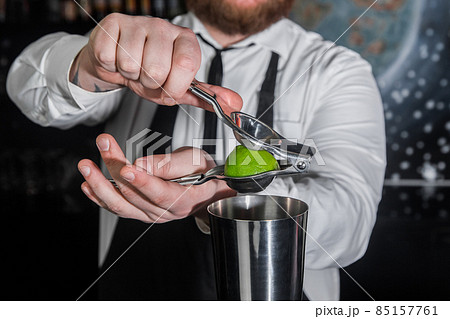 Hands of a professional bartender squeeze lime juice with an iron tool with a juicer into a metal shaker, close-up 85157761