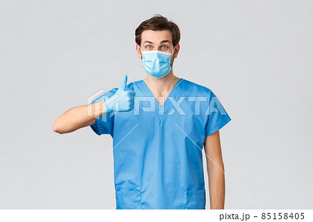 Coronavirus outbreak, healthcare workers fighting disease, hospitals concept. Pleased doctor in medical mask, globes and scrubs, show thumb-up to show support, save people lives, treat patients Coronavirus outbreak, healthcare workers fighting disease, hospitals concept. Pleased doctor in medical mask, globes and scrubs, show thumb-up to show support, save people lives, treat patients 85158405