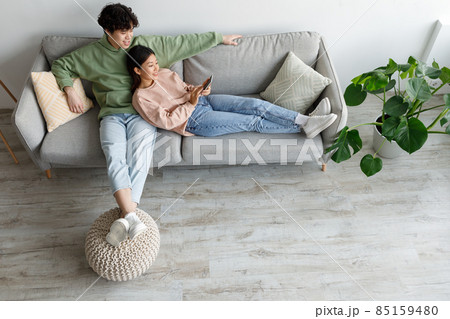 Loving Asian couple using smartphone, surfing internet or watching movie online, resting on sofa indoors, top view Loving Asian couple using smartphone, surfing internet or watching movie online, resting on sofa indoors, top view 85159480