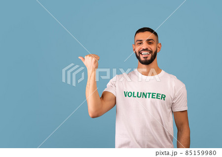 Look there. Happy arab male volunteer pointing aside and smiling, showing empty space, blue background, panorama Look there. Happy arab male volunteer pointing aside and smiling, showing empty space, blue background, panorama 85159980