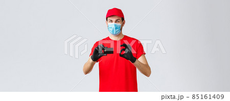Contactless delivery, payment and online shopping during covid-19, self-quarantine. Friendly courier in red uniform, cap and t-shirt, wear face mask and gloves, thumb-up recommend credit card paying Contactless delivery, payment and online shopping during covid-19, self-quarantine. Friendly courier in red uniform, cap and t-shirt, wear face mask and gloves, thumb-up recommend credit card paying 85161409