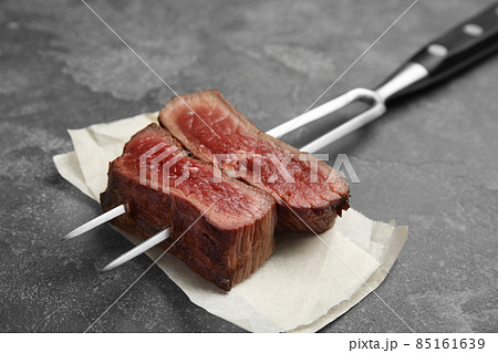 Carving fork with slices of delicious beef steak on grey table, closeup Carving fork with slices of delicious beef steak on grey table, closeup 85161639