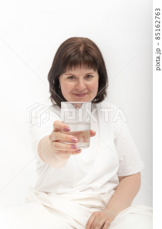 Young dark-haired caucasian girl in white clothes hands you glass of water. Portrait on white background. Vertical frame Young dark-haired caucasian girl in white clothes hands you glass of water. Portrait on white background. Vertical frame 85162763