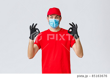 Covid-19, self-quarantine, online shopping and shipping concept. Excited delivery guy in red cap, t-shirt and face mask working coronavirus outbreak, show okay sign, guarantee safe courier service Covid-19, self-quarantine, online shopping and shipping concept. Excited delivery guy in red cap, t-shirt and face mask working coronavirus outbreak, show okay sign, guarantee safe courier service 85163676