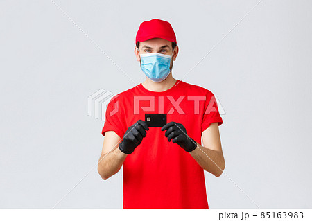 Contactless delivery, payment and online shopping during covid-19, self-quarantine. Cheerful courier in red uniform cap and t-shirt, wear medical face mask, gloves showing credit card, order food Contactless delivery, payment and online shopping during covid-19, self-quarantine. Cheerful courier in red uniform cap and t-shirt, wear medical face mask, gloves showing credit card, order food 85163983