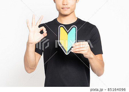 白い背景の前に立って初心者マークを見せる黒いTシャツを着た男性 85164096