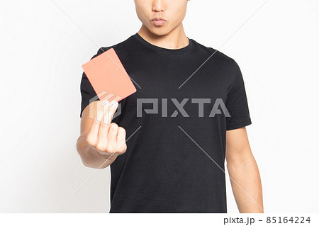 白い背景の前に立ってレッドカードを見せる黒いTシャツを着ている男性 85164224