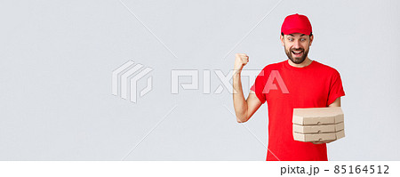 Food delivery, quarantine, stay home and order online concept. Excited and happy courier in red t-shirt and cap, rejoicing holding tasty pizzas, look at boxes and fist pump, grey background 85164512