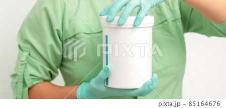 Hands in protective gloves of beautician open a white body cream jar on white background. 85164676