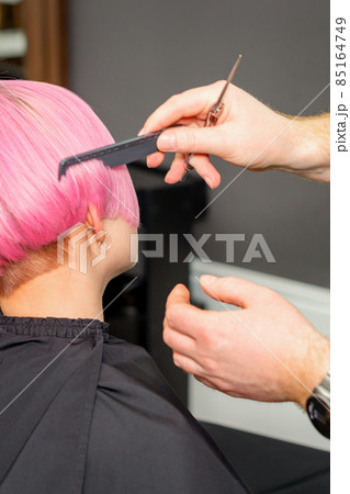 Hands of hairdresser combing hair making short pink hairstyle for a young caucasian woman in a beauty salon. Hands of hairdresser combing hair making short pink hairstyle for a young caucasian woman in a beauty salon. 85164749