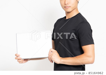白い背景の前に立って小さいスケッチブックを見せる黒いTシャツを着ている男性 85164962