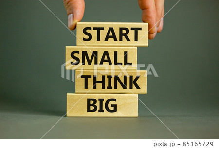 Start small think big symbol. Concept words 'Start small think big' on wooden blocks on a beautiful grey background. Businessman hand. Business, motivational and start small think big concept. 85165729