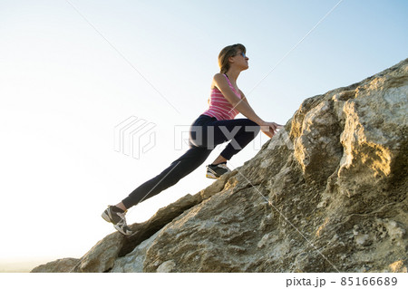 Woman hiker climbing steep big rock on a sunny day. Young female climber overcomes difficult climbing route. Active recreation in nature concept. 85166689