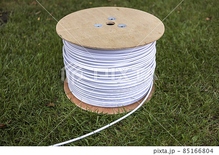 Top view of roll of white industrial electrical cable on large wooden reel isolated outdoors on green grass. Professional construction site cable, reliable wiring and durability. Top view of roll of white industrial electrical cable on large wooden reel isolated outdoors on green grass. Professional construction site cable, reliable wiring and durability. 85166804