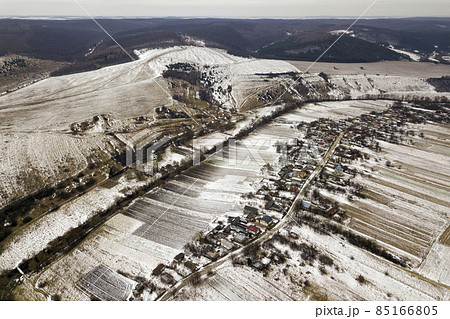 Top view of empty snowy fields, houses along road and woody hills on blue sky background. Aerial drone photography, winter landscape. Top view of empty snowy fields, houses along road and woody hills on blue sky background. Aerial drone photography, winter landscape. 85166805