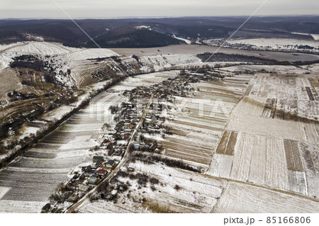 Top view of empty snowy fields, houses along road and woody hills on blue sky background. Aerial drone photography, winter landscape. Top view of empty snowy fields, houses along road and woody hills on blue sky background. Aerial drone photography, winter landscape. 85166806
