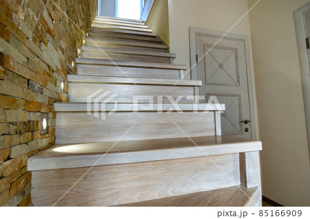 Stylish wooden contemporary staircase inside loft house interior. Modern hallway with decorative limestone brick walls and white oak stairs. 85166909