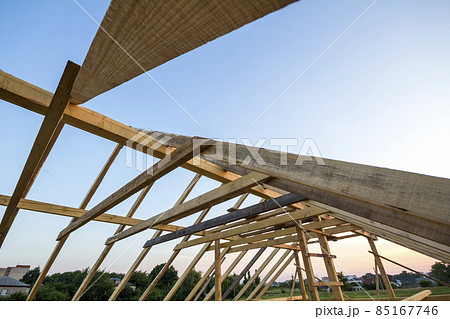 New wooden house under construction. Close-up of attic roof frame against clear sky from inside. Ecological dream home of natural materials. Building, construction and renovation concept. New wooden house under construction. Close-up of attic roof frame against clear sky from inside. Ecological dream home of natural materials. Building, construction and renovation concept. 85167746