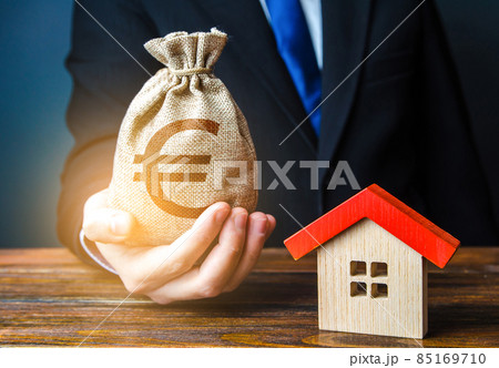 Man holds out a euro bag near the house. Bank approval for issuing a mortgage loan. Home purchase, invest in real estate. Property appraisal. Favorable terms and conditions, low interest rate. Man holds out a euro bag near the house. Bank approval for issuing a mortgage loan. Home purchase, invest in real estate. Property appraisal. Favorable terms and conditions, low interest rate. 85169710