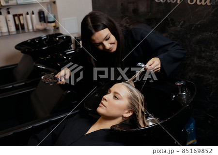 Hairdresser in beauty salon washes his client hair, before procedure of applying natural restoring ingredients and vitamins to hair and haircut. Hairdresser in beauty salon washes his client hair, before procedure of applying natural restoring ingredients and vitamins to hair and haircut. 85169852