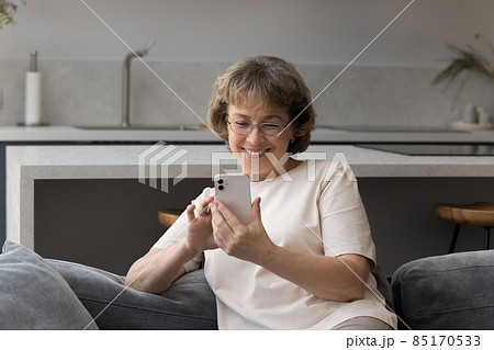 Happy cheerful elder lady in eye glasses reading texting message Happy cheerful elder lady in eye glasses reading texting message 85170533