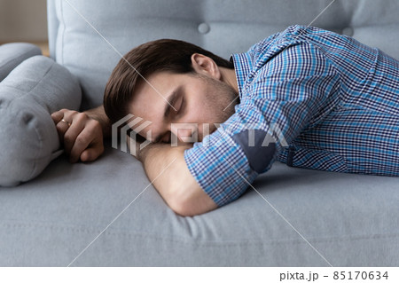 Exhausted young man lying down on sofa Exhausted young man lying down on sofa 85170634