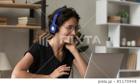 Smiling Latin woman in headphones talk on video call Smiling Latin woman in headphones talk on video call 85170948