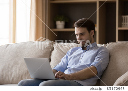 Focused smiling young business man working at laptop from home 85170963