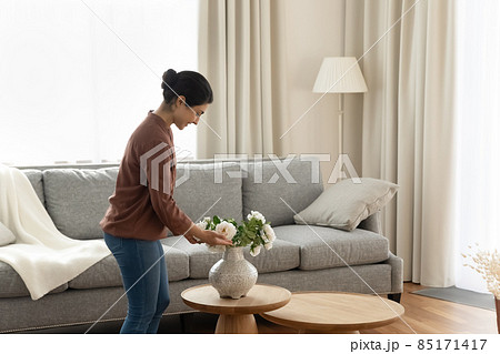 Smiling young indian ethnicity woman putting flowers in vase. Smiling young indian ethnicity woman putting flowers in vase. 85171417
