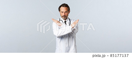 Covid-19, coronavirus outbreak, healthcare workers and pandemic concept. Serious displeased male doctor in white coat, cross hands to show stop gesture, prohibit or forbid smth 85177137