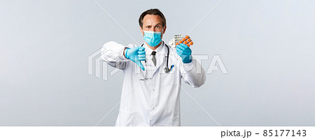 Covid-19, preventing virus, healthcare workers and vaccination concept. Displeased serious doctor in medical mask and gloves, show thumb-down and medication, bad quality pills, wrong prescription Covid-19, preventing virus, healthcare workers and vaccination concept. Displeased serious doctor in medical mask and gloves, show thumb-down and medication, bad quality pills, wrong prescription 85177143