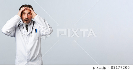 Covid-19, coronavirus outbreak, healthcare workers and pandemic concept. Alarmed anxious male doctor realise making huge mistake, grab head staring in panic, being concerned Covid-19, coronavirus outbreak, healthcare workers and pandemic concept. Alarmed anxious male doctor realise making huge mistake, grab head staring in panic, being concerned 85177206