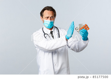 Covid-19, preventing virus, healthcare workers and vaccination concept. Serious displeased doctor prohibit using this pills, showing no or stop gesture as talking about medication, wear medical mask 85177500