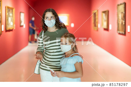Mother and daughter in protective medical masks looking at expositions in museum Mother and daughter in protective medical masks looking at expositions in museum 85178297