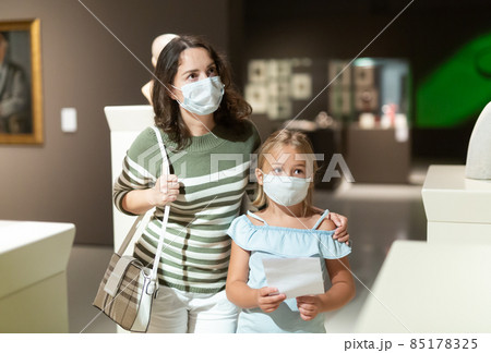 Mother and daughter in masks with guide enjoying expositions in museum Mother and daughter in masks with guide enjoying expositions in museum 85178325
