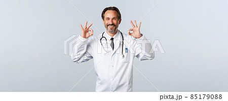 Covid-19, coronavirus outbreak, healthcare workers and pandemic concept. Satisfied happy doctor guarantee quality. Therapist show okay gesture and smiling pleased, advertise promo 85179088