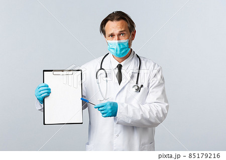 Covid-19, preventing virus, healthcare workers and vaccination concept. Worried and confused male doctor in medical mask and gloves, pointing at clipboard with information or diagnose Covid-19, preventing virus, healthcare workers and vaccination concept. Worried and confused male doctor in medical mask and gloves, pointing at clipboard with information or diagnose 85179216