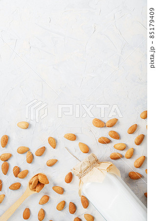 Almond milk in a glass bottle on a light background with a scattering of seed kernels and a wooden spoon. Almond milk in a glass bottle on a light background with a scattering of seed kernels and a wooden spoon. 85179409
