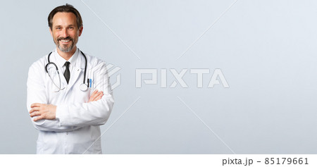 Covid-19, coronavirus outbreak, healthcare workers and pandemic concept. Enthusiastic smiling doctor, physician in white coat looking enthusiastic, cross arms chest, listening to patient Covid-19, coronavirus outbreak, healthcare workers and pandemic concept. Enthusiastic smiling doctor, physician in white coat looking enthusiastic, cross arms chest, listening to patient 85179661