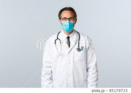 Covid-19, preventing virus, healthcare workers and vaccination concept. Serious confident male doctor in white coat and medical mask, wearing glasses, ready treat patient with influenza 85179715